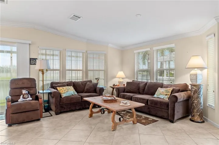 Living room featuring light tile patterned flooring, crown molding, and vaulted ceiling