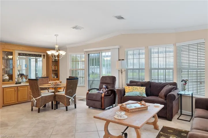 Living room featuring light tile patterned flooring, lofted ceiling, crown molding, and a chandelier