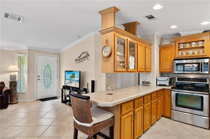 Kitchen featuring light tile patterned flooring, kitchen peninsula, ornamental molding, and appliances with stainless steel finishes