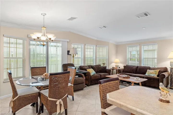 Living room with lofted ceiling, a chandelier, light tile patterned floors, and crown molding