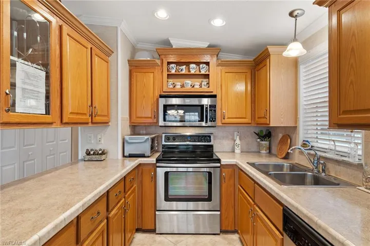 Kitchen with pendant lighting, sink, stainless steel appliances, ornamental molding, and light tile patterned floors