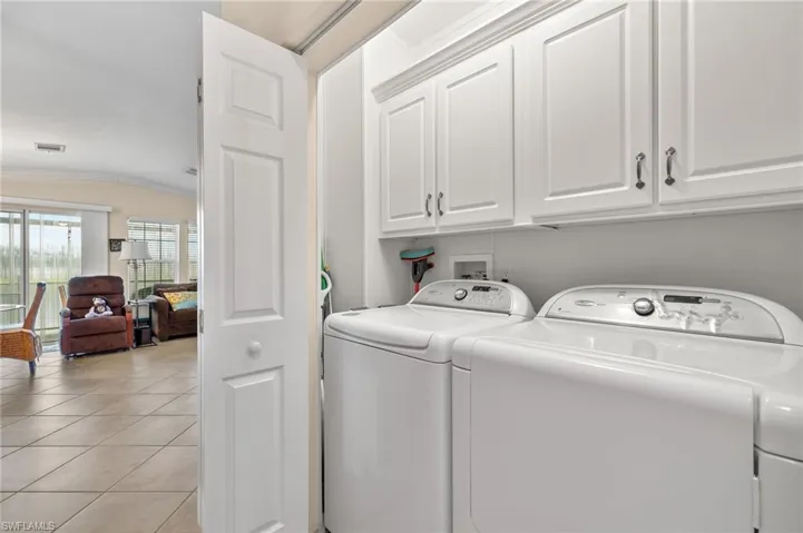 Washroom featuring ornamental molding, cabinets, light tile patterned floors, and washing machine and clothes dryer