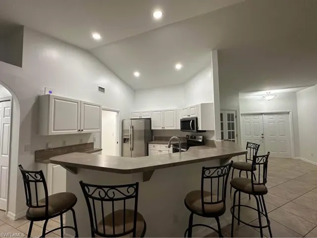 Kitchen featuring light tile patterned floors, dark countertops, stainless steel appliances, a kitchen breakfast bar, and white cabinets