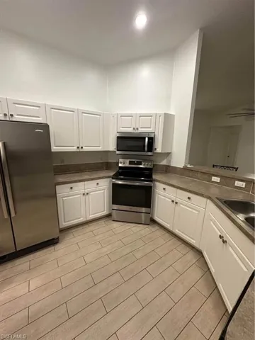 Kitchen with stainless steel appliances, white cabinets, dark countertops, and recessed lighting