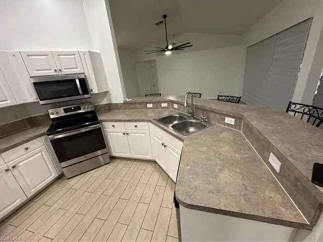 Kitchen with stainless steel appliances, white cabinets, lofted ceiling, a peninsula, and wood finish floors