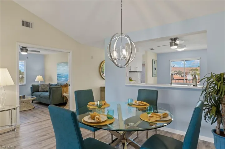 Dining area with ceiling fan with notable chandelier, vaulted ceiling, and light hardwood / wood-style flooring