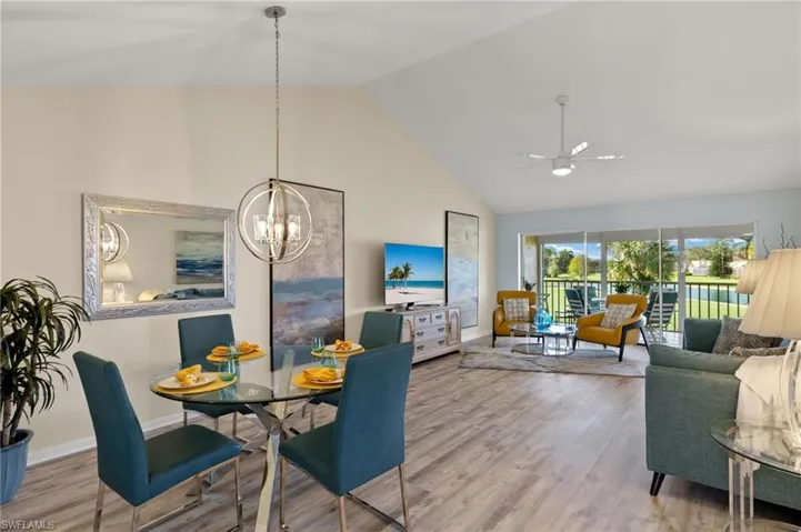 Dining room with ceiling fan with notable chandelier, light hardwood / wood-style floors, and high vaulted ceiling