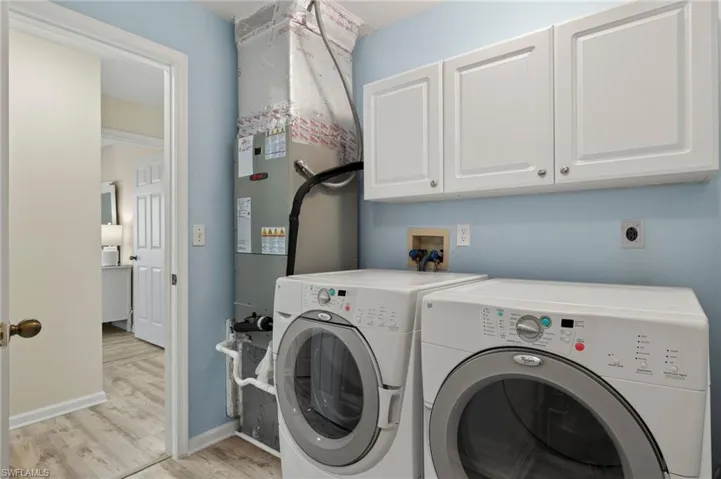 Clothes washing area with cabinets, washing machine and dryer, and light hardwood / wood-style flooring
