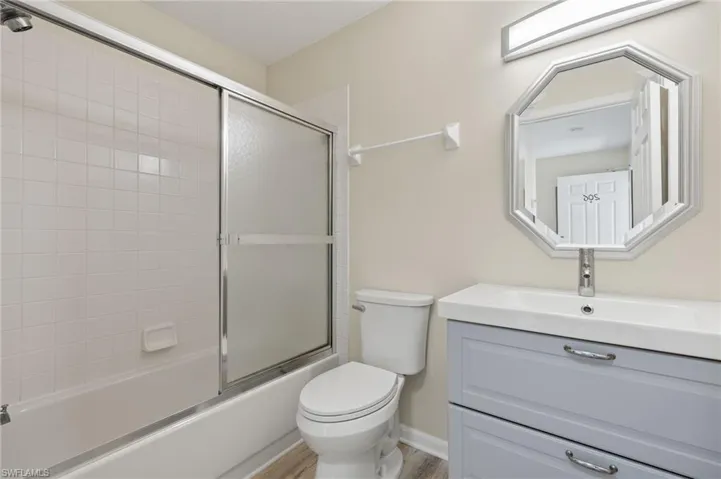 Full bathroom featuring vanity, toilet, wood-type flooring, and bath / shower combo with glass door