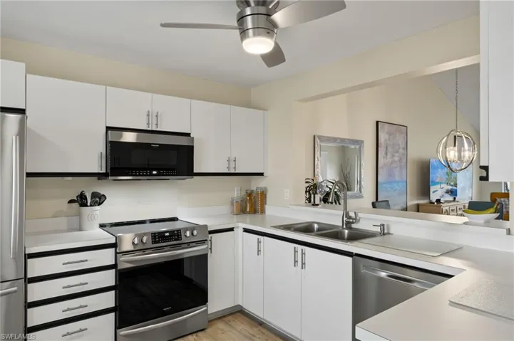 Kitchen featuring appliances with stainless steel finishes, sink, pendant lighting, light hardwood / wood-style flooring, and white cabinetry