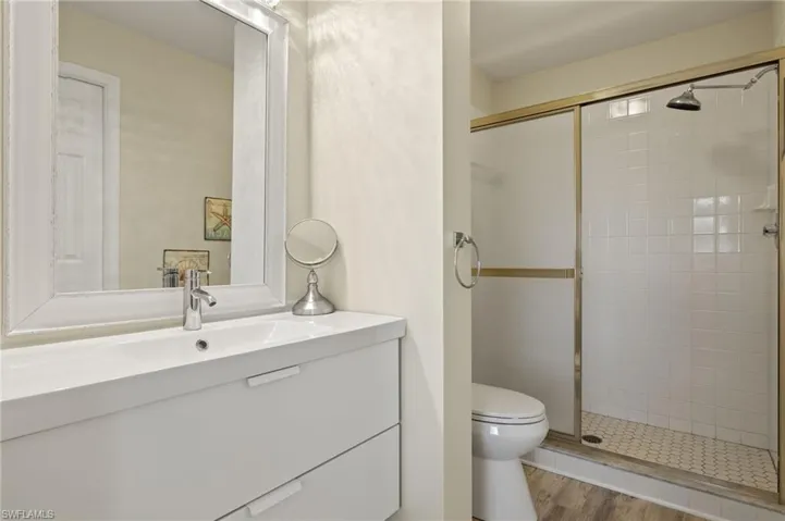 Bathroom with hardwood / wood-style floors, vanity, toilet, and a shower with shower door