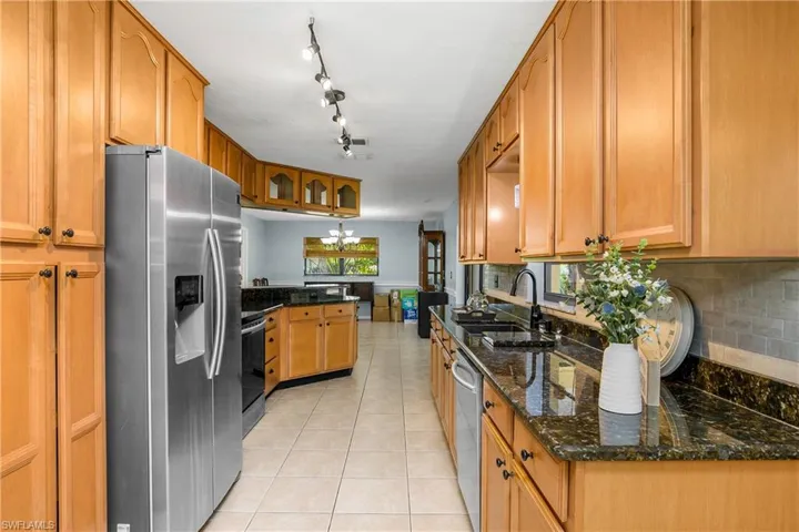 Kitchen featuring appliances with stainless steel finishes, light tile patterned floors, a peninsula, tasteful backsplash, and dark stone counters