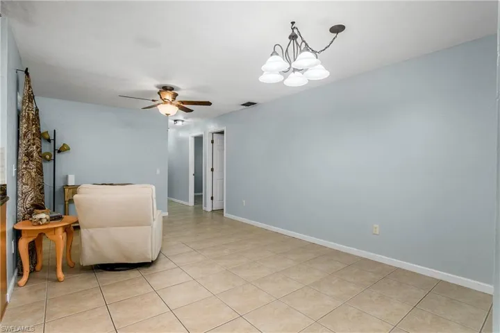 Family room area with light tile patterned floors, a ceiling fan, and a chandelier