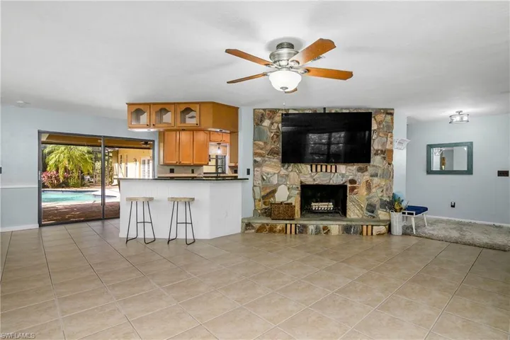 Living room featuring light tile patterned floors, a ceiling fan, and a stone fireplace