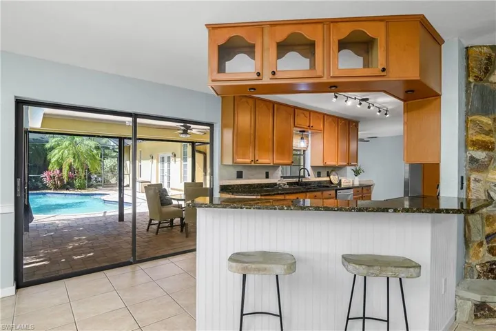 Kitchen featuring dark stone counters, stainless steel dishwasher, glass insert cabinets, and rail lighting