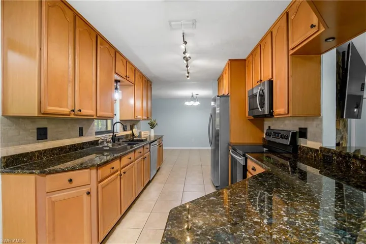Kitchen with stainless steel appliances, rail lighting, light tile patterned flooring, tasteful backsplash, and dark stone countertops
