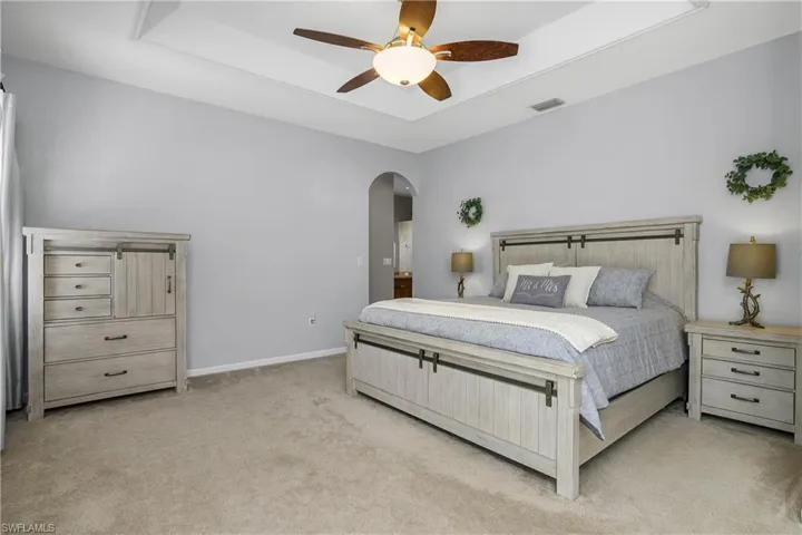 Master Bedroom with arched walkways, light carpet, a raised ceiling, and a ceiling fan