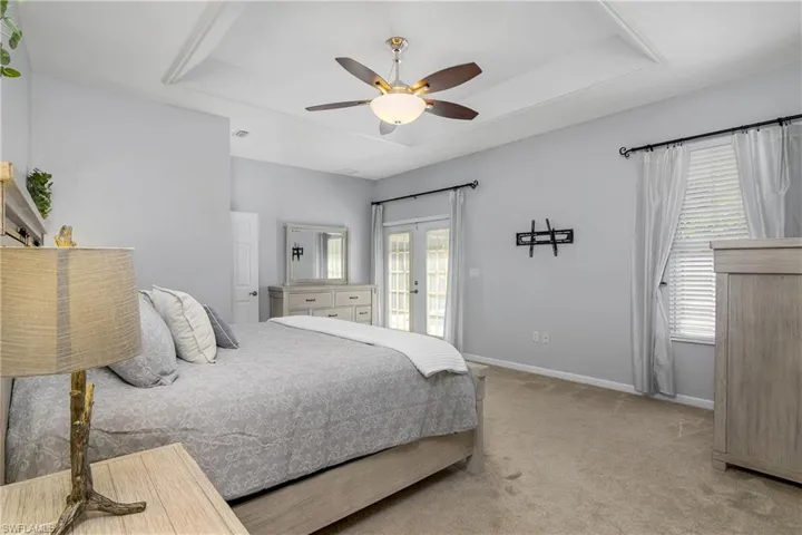 Master bedroom featuring a tray ceiling, french doors, a ceiling fan, and access to exterior