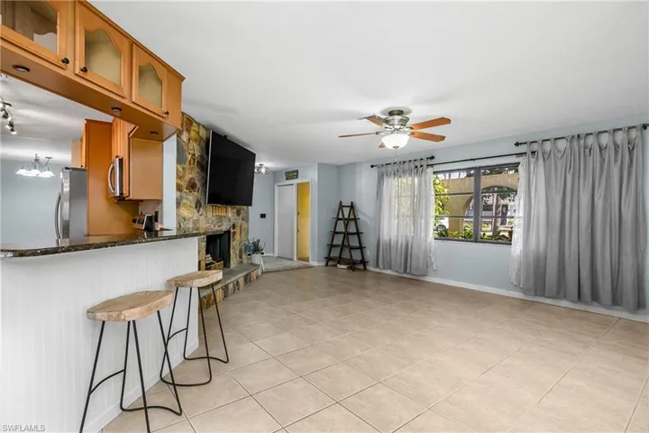 Kitchen with stainless steel appliances, a ceiling fan, brown cabinets, light tile patterned flooring, and glass insert cabinets