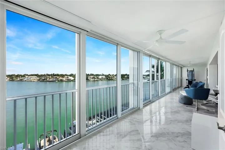 Sunroom with marble tiled flooring, a water view, and a wall of windows