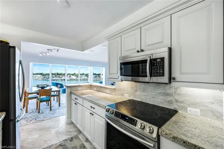 Kitchen featuring stainless steel appliances, light stone counters, light marble finish flooring, white cabinetry, and a water view