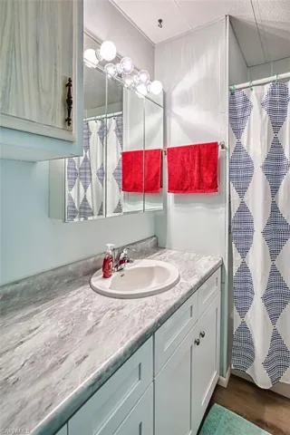 Full bath with curtained shower, vanity, and dark wood finished floors