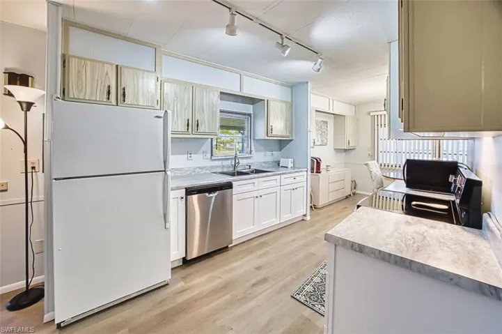 Kitchen featuring freestanding refrigerator, light countertops, stainless steel dishwasher, light wood-style flooring, and rail lighting