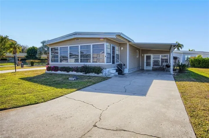 View of front facade featuring a front lawn, driveway, an attached carport, and a sunroom