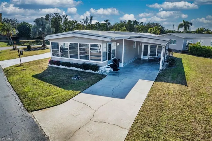 Manufactured / mobile home featuring driveway, a front lawn, a carport, and a sunroom