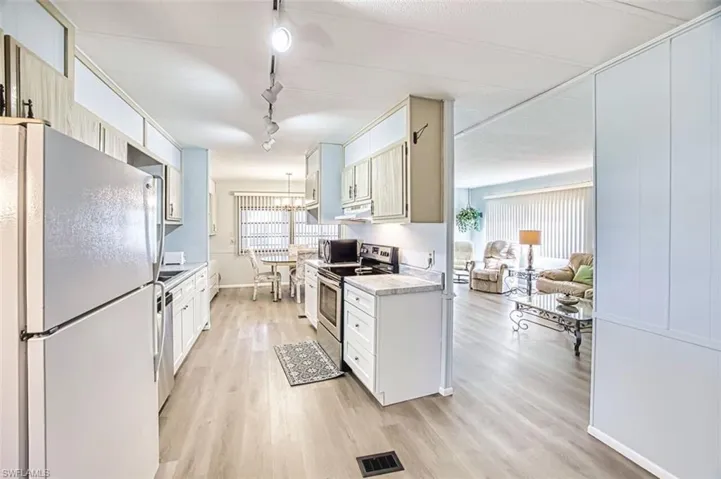 Kitchen with stainless steel appliances, light countertops, light wood finished floors, track lighting, and white cabinetry