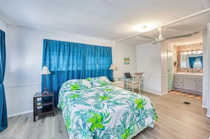 Bedroom with light wood finished floors, ceiling fan, ensuite bath, and a textured ceiling