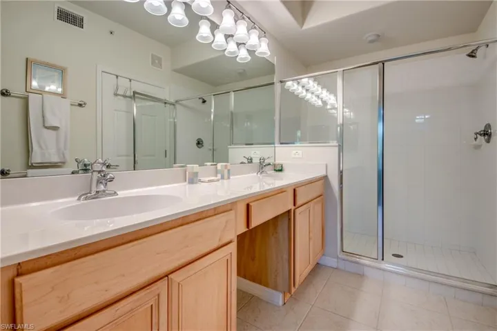 Bathroom featuring tile patterned flooring, a shower with shower door, and dual bowl vanity