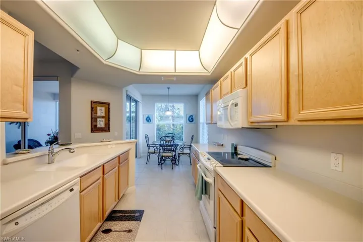 Kitchen with sink, light tile patterned floors, light brown cabinetry, and white appliances