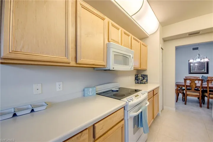 Kitchen featuring decorative light fixtures, a chandelier, light brown cabinets, white appliances, and light tile patterned floors