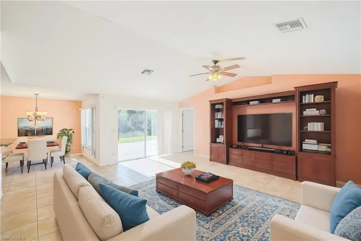Tiled living room with vaulted ceiling and ceiling fan with notable chandelier (This photo was virtually staged)