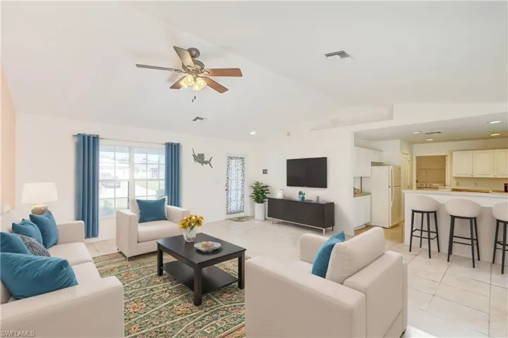 Living room featuring ceiling fan, vaulted ceiling, and light tile patterned floors (This photo was virtually staged)