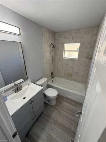 Bathroom featuring a white vanity with integrated sink, rectangular mirror, tile-surround bathtub/shower combination, and wood-look tile flooring