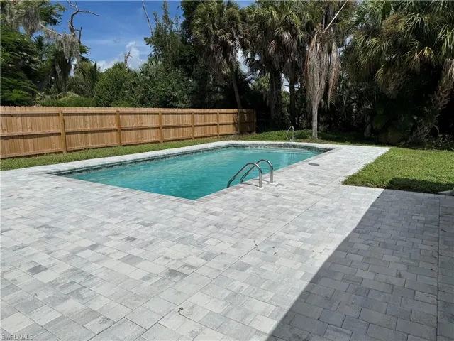 Swimming pool with integrated steps, surrounded by light-toned paver decking, a privacy fence, and mature trees