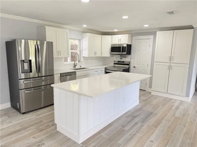 Modern kitchen featuring white shaker cabinetry, stainless steel appliances, a center island with counter seating, light-toned countertops, and wood-finish flooring