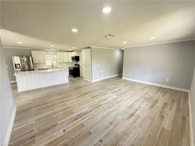 Open-concept living space with wood-finish flooring, recessed lighting, and crown molding