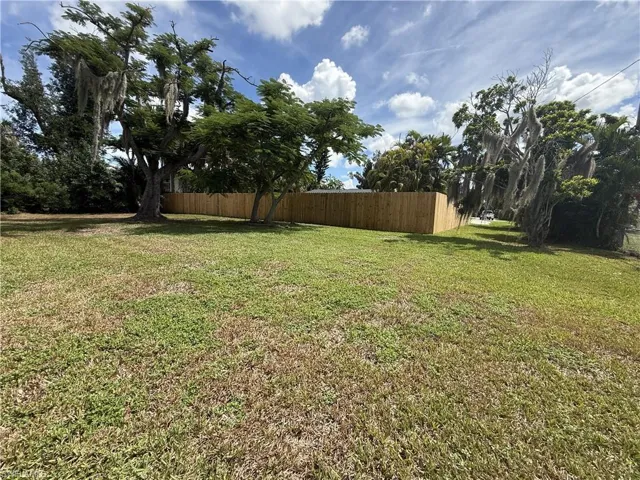 Grassy lot featuring mature trees and a wood privacy fence