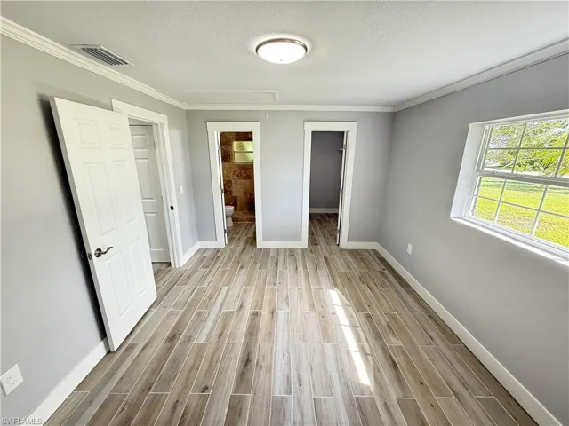Wood-finish plank flooring, crown molding, white trim, and a ceiling-mounted light fixture