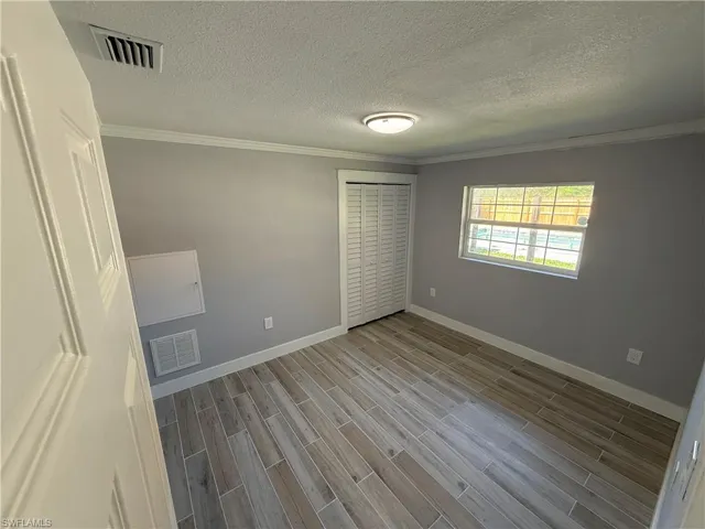 Wood-finish flooring, crown molding, flush mount lighting, louvered closet doors, and a window with a fenced yard beyond