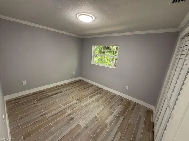 Wood-finish plank flooring, crown molding, and a built-in closet with louvered bifold doors