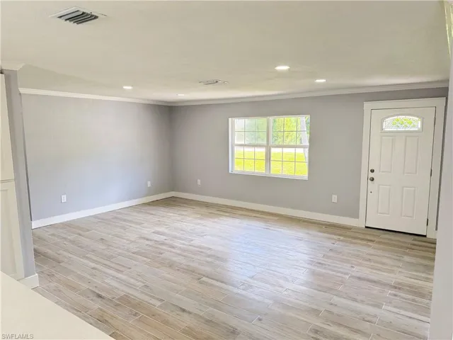 Recessed lighting, wood-finish flooring, crown molding, and a white paneled entry door with an arched glass insert