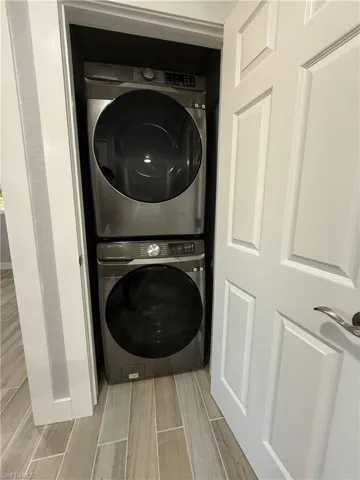 Stacked laundry appliances within a dedicated closet, featuring a paneled door and wood-finish tile flooring