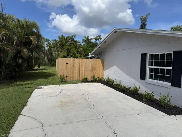 Exterior featuring a concrete driveway, a privacy fence, a window with black shutters, and landscaping
