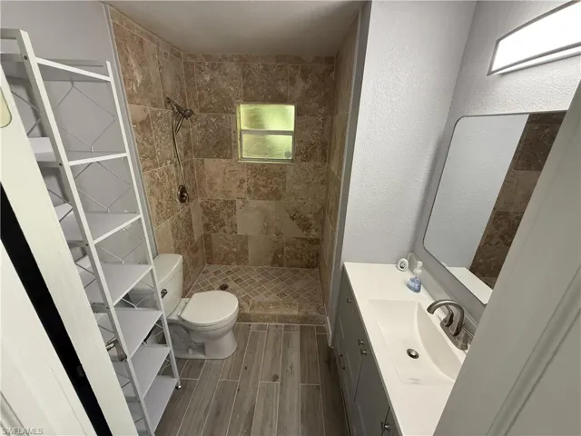 Walk-in shower with tiled surround, wood-finish flooring, vanity with integrated sink, and illuminated mirror