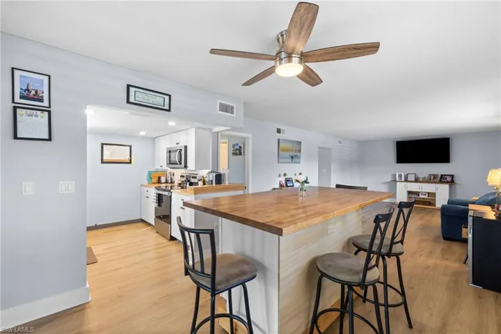 Kitchen with a kitchen breakfast bar, white cabinetry, butcher block countertops, stainless steel appliances, and light wood-style flooring