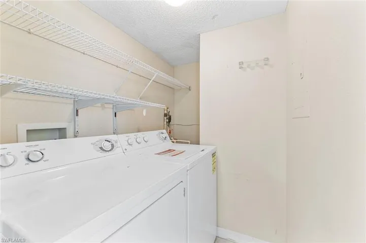 Dedicated laundry area featuring white wall shelving, a washer and dryer, water heater, and additional storage